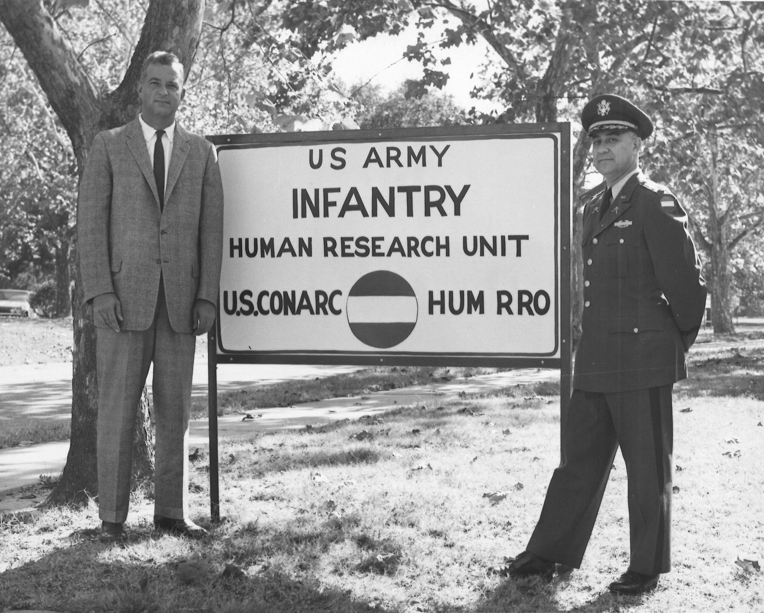 Image of two men in front of a sign that says "U.S. Army Infantry Human Research Unit U.S.Conarc HumRRO"
